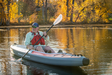 man wearing lifejacket paddling on a lake in autumn