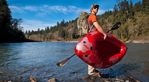 man holding inflatable kayak and paddle looking back