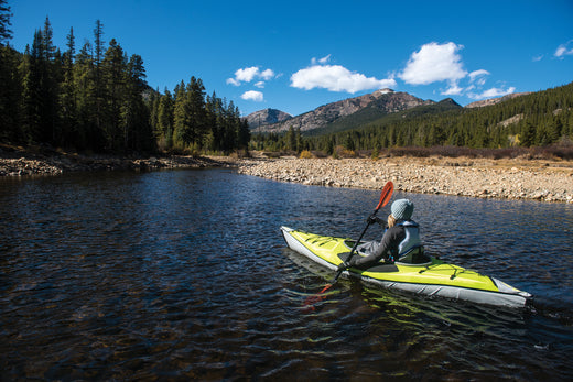 woman wearing a beanie paddling a kayak on a calm river