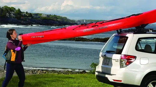 Woman loading kayak onto a roof rack on car