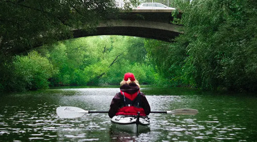 woman floating in kayak on calm river under bridge