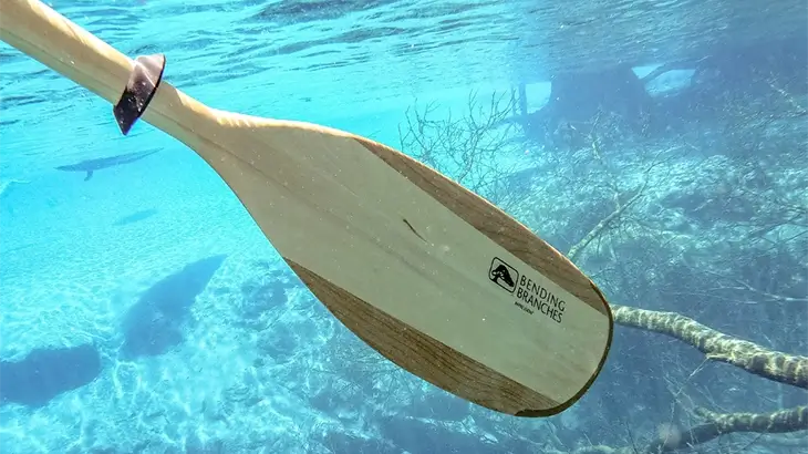 Wooden kayak paddle going through the water