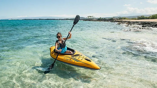 woman paddling inflatable kayak on clear ocean water near the beach