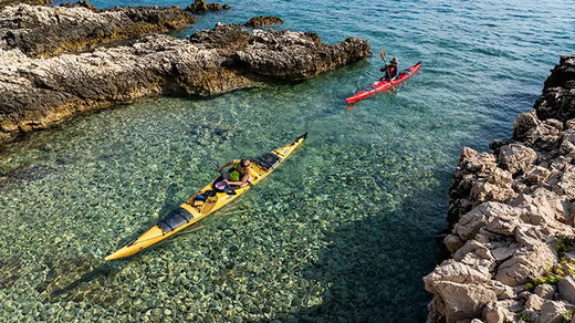two paddlers in long sea kayaks between rock formations