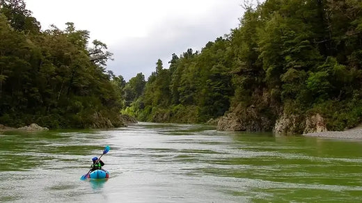 person paddling a kayak on a green river surrounded by trees