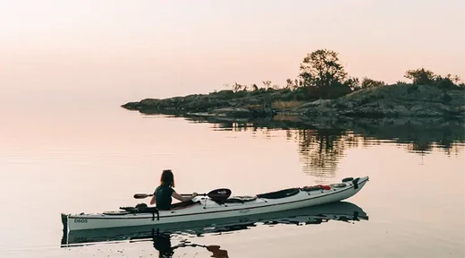 person solo paddling a tandem kayak at sunset