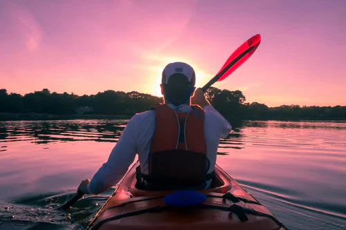 Man paddling a kayak into the sunset