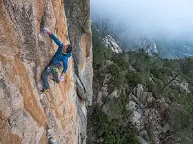 Man rock climbing above trees and rocks