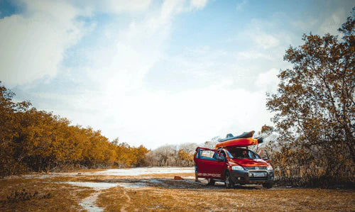 red car with kayak on roof rack in a field